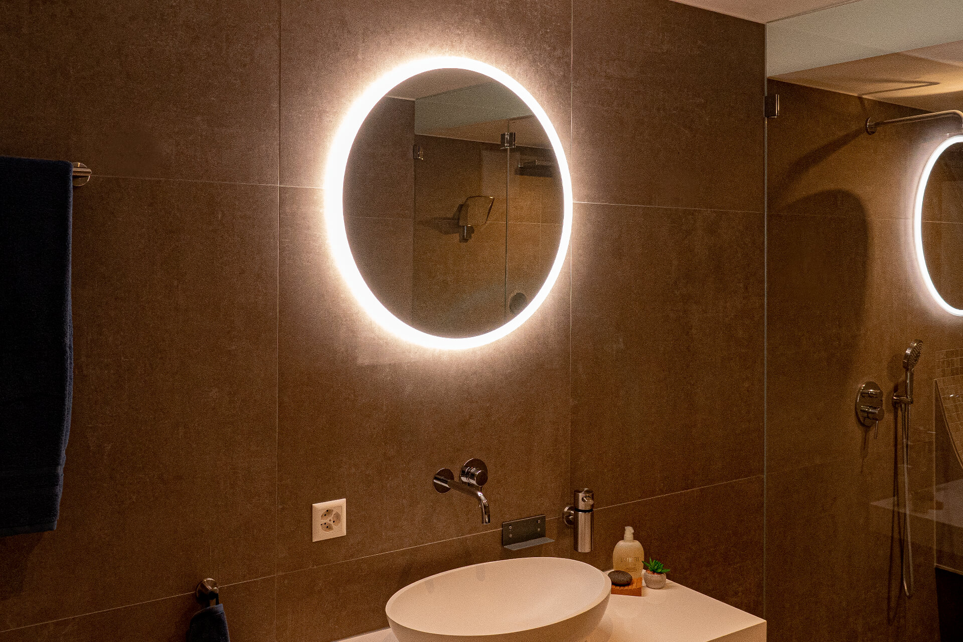 Round mirror with backlighting, washbasin and shower.