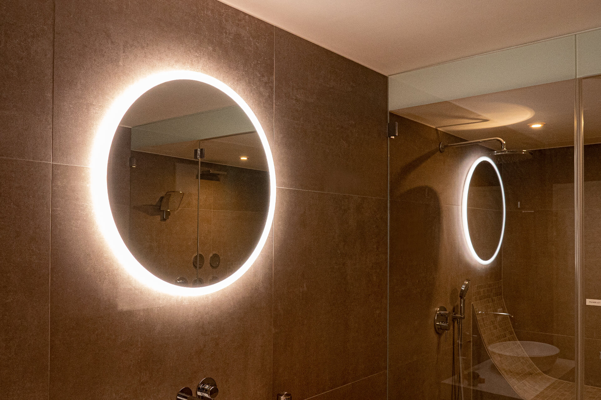 Round mirror with backlighting with reflection in glass wall shower.